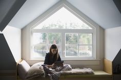 a woman sitting on top of a bed under a window next to a white blanket