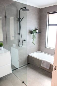 a bathroom with a glass shower door and white tub next to a window in the corner