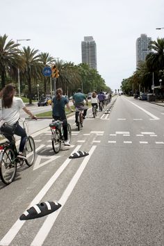 several people riding bicycles down the street with palm trees in the backgrouds