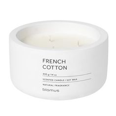 a white candle sitting inside of a glass container on top of a white surface with the words, french cotton