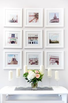 a white table with flowers and candles on it in front of some framed pictures hanging on the wall