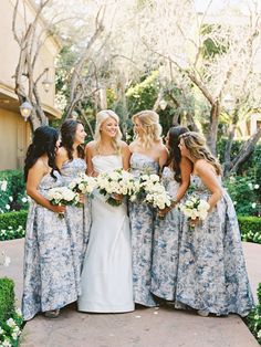 a group of women standing next to each other wearing dresses and holding bouquets in their hands