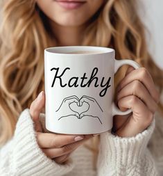 a woman holding a white coffee mug with the word kathy written in black on it