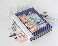 an open book with scissors and other crafting items around it on a white surface