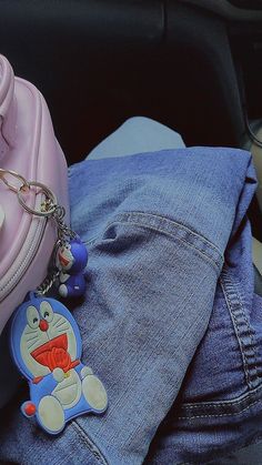 a pink purse with a cat keychain on it sitting next to some jeans