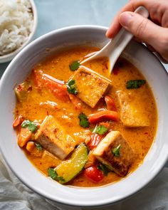 a bowl filled with tofu and vegetables next to rice on a blue table cloth