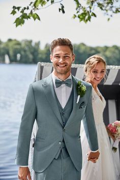 a bride and groom holding hands while standing next to each other on a dock near the water