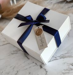 a white gift box with a blue ribbon and a tag on it sitting on a marble surface