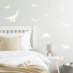 a white bed sitting next to a wall with dinosaurs on it