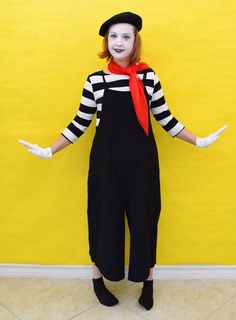 a woman dressed as a clown standing in front of a yellow wall with her hands out