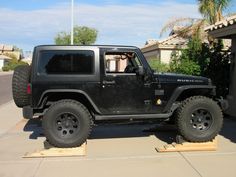 a black jeep is parked in front of a house with two wooden boards on the ground