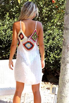 a woman standing next to a tree wearing a white dress with multicolored beads