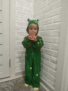 a little boy dressed as a frog standing in front of a brick wall with his hands together