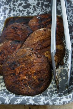 some meat is in a pan with tongs