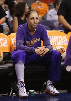 a man sitting on top of a bench in front of a basketball court with other people watching