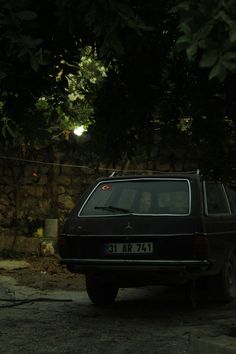 an old car parked in front of a stone wall and tree with lights shining on it