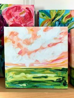 three colorful paintings sitting on top of a wooden shelf