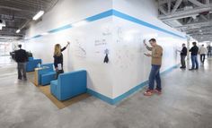 several people are writing on the wall in an open space with blue and white chairs