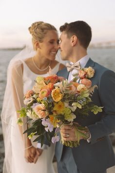 a bride and groom standing next to each other near the water with their wedding bouquet