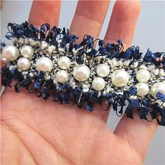 a hand is holding a blue and white beaded hair clip with pearls on it