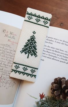 a cross stitch bookmark with a christmas tree on it next to a pine cone