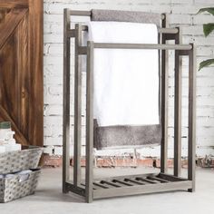 a towel rack in front of a brick wall with a plant and basket on the floor