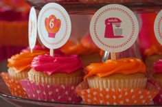 cupcakes with pink and orange frosting sitting on top of a cake plate