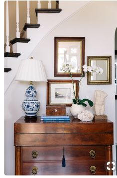 a wooden dresser topped with vases and flowers next to a stair case filled with framed pictures