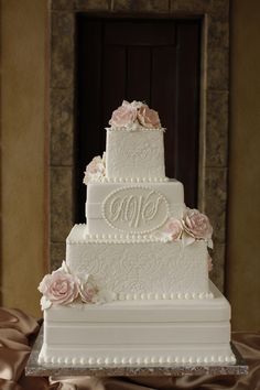 a three tiered white wedding cake with pink flowers on top and the word monogram