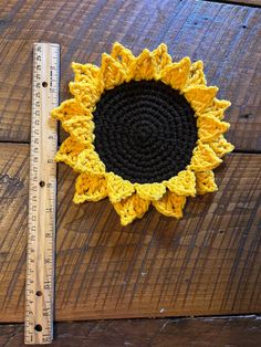 a crocheted sunflower sits next to a ruler on a wooden surface,