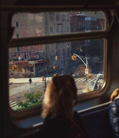 a woman looking out the window of a bus at an intersection with traffic lights and buildings