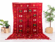 a large red rug is sitting on the floor next to a potted plant and some plants