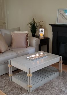 a coffee table with candles on it in front of a couch and fire place next to a fireplace