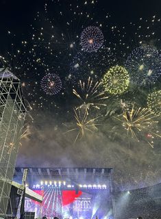 fireworks are lit up in the night sky above a crowd at a music festival with people watching