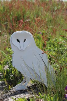 a white owl statue sitting on top of a rock in the middle of some grass