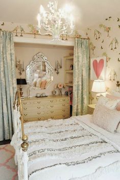 a white bed sitting under a chandelier in a bedroom next to a window