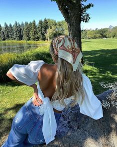 a woman sitting on top of a rock next to a tree wearing a bandana