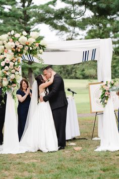 a bride and groom kissing under an arch at their outdoor wedding ceremony in the park