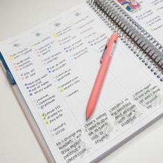 a spiral notebook with a pink pen on top of it next to an open planner