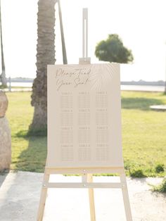 an easel with a seating chart on it in front of palm trees and grass