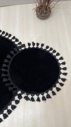 two round black rugs with tassels on the floor next to a potted plant