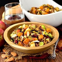 a wooden bowl filled with fruit and nuts next to another bowl full of food on a table