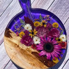 a purple vase filled with lots of flowers on top of a wooden table next to a cutting board