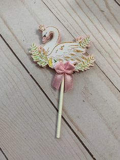 a white swan lollipop with a pink bow on it's head sitting on top of a wooden floor