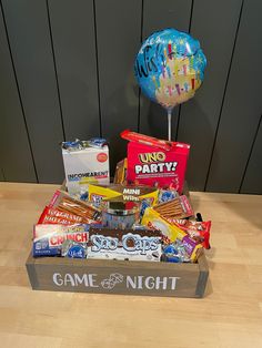 a game night box filled with candy, snacks and balloons on top of a wooden table