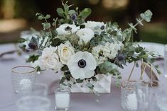 a vase filled with white and pink flowers sitting on top of a table covered in candles