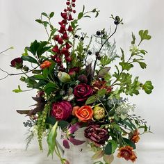 a vase filled with lots of different colored flowers and greenery next to a white wall