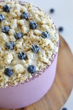 there is a cake with blueberries and cream on the top it sits on a wooden platter