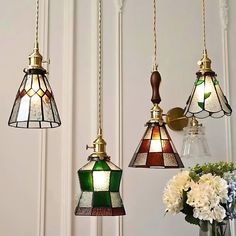 three stained glass lamps hanging from the ceiling in front of a vase with white flowers