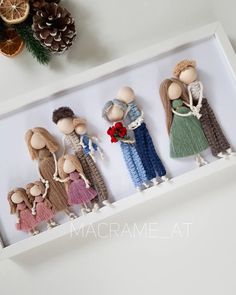 three wooden dolls in a white box with pine cones